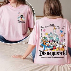 May include: Pink t-shirt featuring Mickey Mouse and the word "Daddy" on the front. The back of the shirt displays a Disneyworld graphic with various cartoon characters and the text "Disneyworld - 1971".