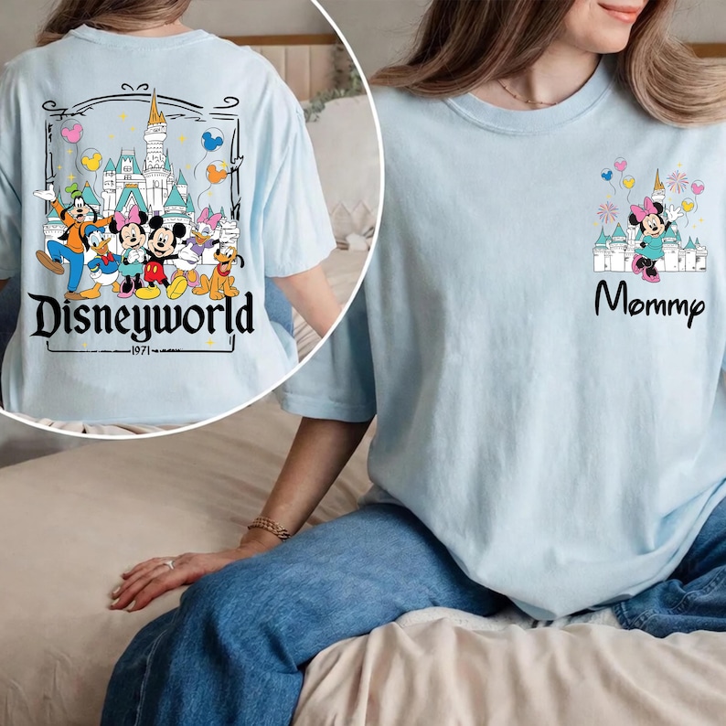 May include: Light blue t-shirts with Disney character graphics. One shirt features "Disneyworld" with characters and a castle, the other says "Mommy" with Minnie Mouse and a castle. Both shirts have a relaxed fit.