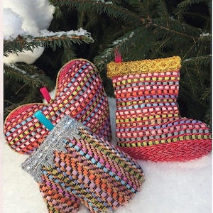 May include: Colorful woven mittens and a boot-shaped ornament with a gold trim, set against a snowy backdrop with evergreen branches. The mittens and ornament are in shades of pink, orange, yellow, and blue.