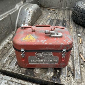 May include: A rectangular red metal gasoline container with a top handle, a silver cap, and two metal latches on the front. The container features a yellow flammable warning triangle and a silver label with the text CAUTION GASOLINE.