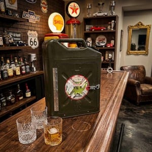 May include: An olive green metal jerry can repurposed as a cabinet, featuring a circular Sinclair Dino gasoline sticker on the front, a silver metal hinge, and a latch. Three clear glass tumblers sit nearby, one containing amber liquid and ice.