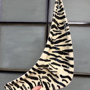 May include: A decorative, crescent-shaped ceramic platter with a zebra stripe pattern in black and cream. The platter has a glossy finish and is held by a hand.