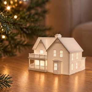 May include: A white ceramic miniature house figurine with a detailed roof, multiple windows, and a balcony. The structure is illuminated from within, casting a warm glow through the window openings, creating a soft light effect.