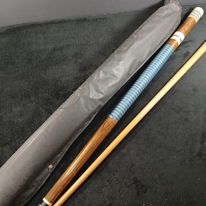 May include: A pool cue with a blue and white grip, a wooden shaft, and a leather case. The cue has a dark wood finish with white and silver accents. The cue is approximately 58 inches long.