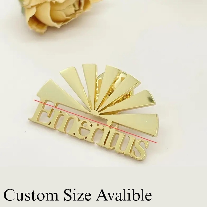 K&ouml;nnte beinhalten: Eine goldfarbene Anstecknadel mit dem Wort "Emeritus" in einer stilisierten Schriftart. Die Anstecknadel hat ein Sonnenstrahl-Design hinter dem Text. Der Text "Custom Size Avalible" steht unter der Anstecknadel.