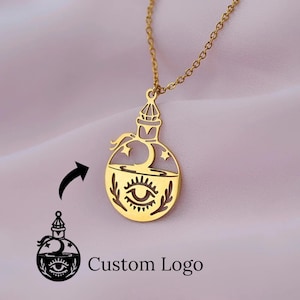 Op de afbeelding: Een goudkleurige hangerketting met een gestileerd drankflesontwerp. De fles heeft een halve maan en sterren, met een oogsymbool aan de onderkant. De tekst "Custom Logo" staat eronder.