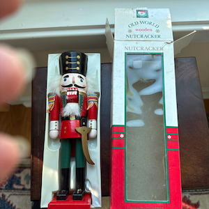 Könnte beinhalten: Eine hölzerne Nussknacker-Figur mit schwarzem Hut, roter Jacke und grüner Hose sowie weißem Haar und Bart. Sie wird neben ihrer originalen weiß-roten Pappschachtel mit der Aufschrift OLD WORLD wooden NUTCRACKER präsentiert.