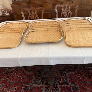 以下が含まれることがあります： 丸みを帯びた角とハンドルが付いた、長方形の織り竹トレイのコレクション。 トレイは白いテーブルクロスの上に配置され、自然な淡い茶色と複雑な織り模様が示されています。 食事や飲み物の提供に最適です。