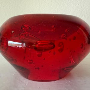 May include: A vibrant red glass bowl with a rounded shape. The bowl has a smooth, glossy surface and is filled with small air bubbles. The bowl is a decorative item.