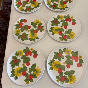 May include: A set of six round white ceramic plates, each featuring a repeating pattern of red strawberries, green leaves, and yellow flowers. The botanical design is distributed across the surface of every plate in this matching dinnerware collection.