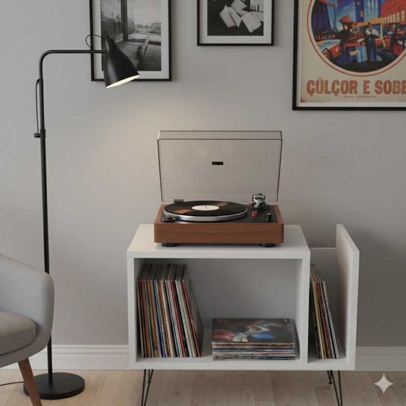 May include: A mid-century modern record player with a wooden base and clear cover sits atop a white storage unit. The unit holds vinyl records. A black floor lamp with an adjustable head is positioned to the left. Artwork hangs on the wall.