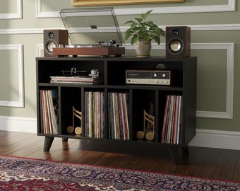 May include: A black record player console with a turntable, speakers, and a vintage stereo receiver. The console has multiple compartments filled with vinyl records and decorative musical note cutouts. A potted plant sits on top.