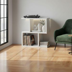 May include: A white, modern side table with a built-in shelf and a turntable on top. The shelf displays vinyl records, decorative vases, and books. The table is next to a green armchair and a window.