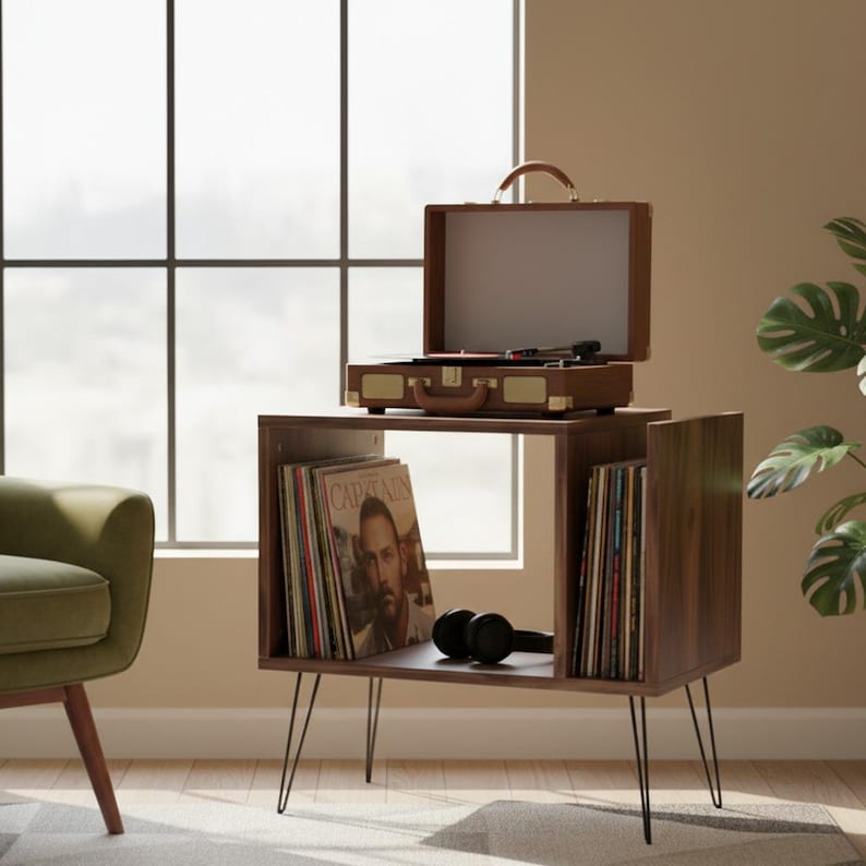May include: A mid-century modern record player stand with a brown finish. The stand features a built-in record storage compartment and a vintage-style record player on top. Black headphones rest on the shelf. The stand has black hairpin legs.