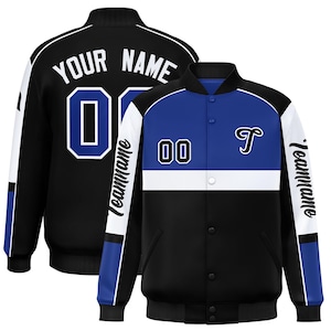 Könnte beinhalten: Schwarz-blaue und weiße Collegejacke mit dem Text "YOUR NAME" und der Nummer "00" auf dem Rücken. Auf der Vorderseite befinden sich die Nummer "00" und der Buchstabe "T". Die Ärmel tragen das Wort "Teamname".