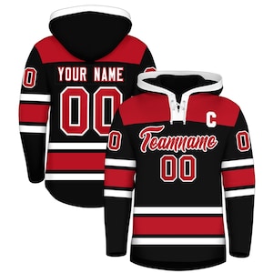 Op de afbeelding: Twee zwarte en rode hockeytruien met witte accenten. Eén trui heeft "YOUR NAME" en het nummer "00" op de rug. De andere trui heeft "Teamname" en het nummer "00" op de voorkant. Beide truien hebben een capuchon.