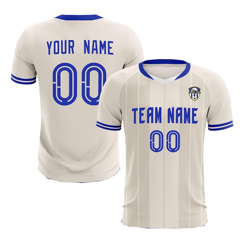 May include: Two cream-colored soccer jerseys with blue accents. One jersey displays "YOUR NAME" and "00" on the back. The other jersey shows "TEAM NAME" and "00" on the front. Both jerseys have a blue collar and sleeve trim.