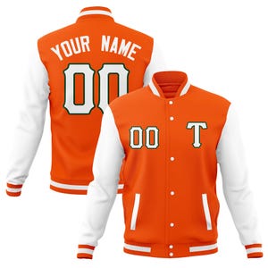 May include: Orange and white varsity jacket with the text "YOUR NAME" and the number "00" on the back. The front of the jacket has the number "00" and the letter "T". The jacket has white sleeves and a white collar.
