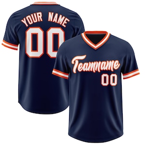 May include: Navy blue baseball jersey with orange and white accents. The jersey features the text "Your Name" and the number "00" on the back. The front displays "Teamname" and the number "00".