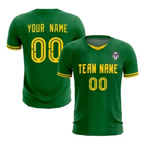 May include: Green soccer jersey with yellow accents. The front displays "TEAM NAME" and the number "00" in yellow. The back of the jersey shows "YOUR NAME" and the number "00". A team logo is on the upper chest.
