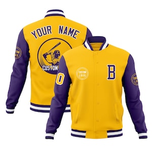 May include: Yellow and purple baseball jacket with white trim. The jacket features the text "YOUR NAME" on the back, a baseball player graphic, and the letter "B" on the front. The sleeves are purple with a white and purple striped cuff.