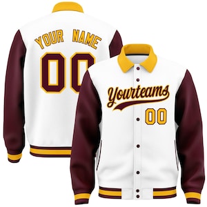 Puede incluir: Una chaqueta universitaria blanca con mangas granates y cuello, puños y dobladillo amarillos. El frente presenta el texto "Yourteams" y el número "00". La parte posterior muestra el texto "YOUR NAME" sobre el número "00" grande en granate y amarillo.