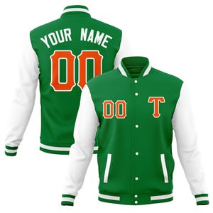 May include: Green and white varsity jacket with orange accents. The jacket features the text "YOUR NAME" and the number "00" on the back. The front of the jacket displays the number "00" and the letter "T".