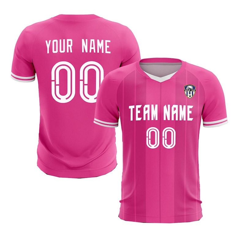 May include: Two pink soccer jerseys. One shows the back with "YOUR NAME" and the number "00" in white. The other jersey shows the front with "TEAM NAME" and "00" in white, plus a team logo. Both have white and black trim.