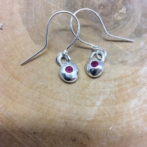 May include: A pair of silver earrings with a small, round, pink gemstone in the center of each earring.