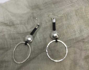 May include: A pair of silver earrings with a hammered circle pendant and a small silver ball hanging from a black leather cord.