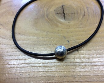 May include: A silver pendant necklace with a hammered, round charm on a black cord.