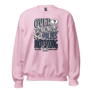 May include: A light pink sweatshirt with the text "OVERTHINKING SOLVES NOTHING BUT ACTION BRINGS CLARITY" in a black and white graphic design. The design includes cartoon robots and a question mark.