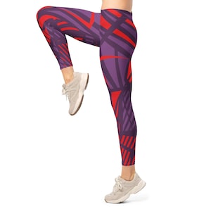 May include: Purple leggings with a red geometric pattern. The leggings are mid-calf length and are being worn with gray athletic shoes. The design features a mix of straight and angled lines.