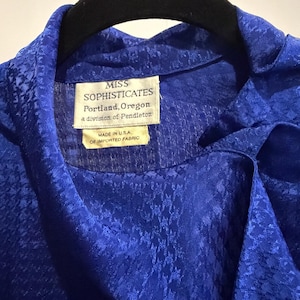 May include: A close-up of a vibrant blue blouse with a textured pattern. The label reads "MISS SOPHISTICATES Portland, Oregon a division of Pendleton MADE IN U.S.A. OF IMPORTED FABRIC."