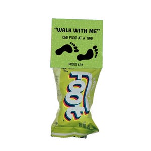 May include: A green package of fruit snacks with the word "Foot" in large, colorful letters. A green tag at the top reads "WALK WITH ME" and "ONE FOOT AT A TIME" with black footprints and the text "MOSES 6:34".