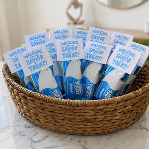 May include: A woven basket filled with multiple individually wrapped Rice Krispies Treats. Each snack is topped with a white cardstock tag featuring blue text that reads Walking With The Savior Is A Treat! accented with small pink and blue stars.