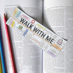 May include: A decorative bookmark with the words "WALK WITH ME" and biblical references. A pink pencil and a yellow pencil rest on the open book.