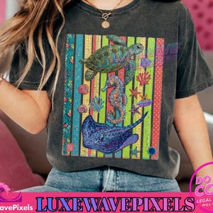 May include: Dark gray t-shirt featuring a colorful graphic of sea creatures including a turtle, seahorse, and stingray. The design is set against a striped background with floral accents, creating a vibrant, ocean-themed design.