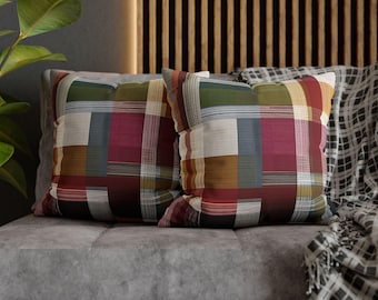 Puede incluir: Dos cojines cuadrados con un diseño de patchwork. Los cojines presentan una mezcla de colores que incluyen rojo, verde, blanco y marrón. Se colocan sobre un sofá gris, con una manta estampada visible en el fondo.