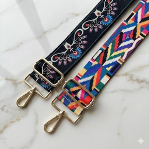 May include: Two adjustable bag straps with gold-tone metal hardware and lobster claw clasps. One strap features a black background with a white, blue, and red floral pattern. The other strap displays a vibrant geometric pattern in red, blue, yellow, and green.
