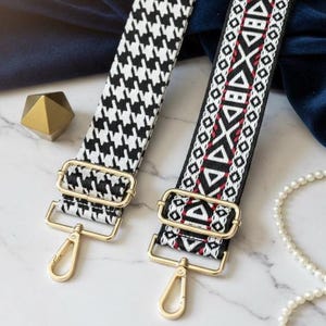 May include: Two adjustable bag straps with gold-tone metal hardware and lobster claw clasps. One strap features a black and white houndstooth pattern, while the other displays a black, white, and red geometric design with repeating triangles.
