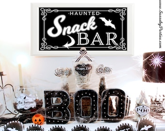以下が含まれることがあります： 黒と白のストライプの旗で飾られたハロウィンのスナックバーテーブル。'BOO'の看板と、'Dragon Eyes'、'Cursed Cat Foetuses'、'Ghost Poo'とラベル付けされたキャンディーの瓶があります。