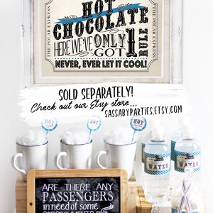 May include: A Polar Express themed hot chocolate bar with a sign that reads "Hot Chocolate Here We've Only Got One Rule Never, Ever Let It Cool!"  The bar includes mugs, marshmallows, candy canes, and water bottles.  A chalkboard sign reads "Are There Any Passengers In Need Of Some Refreshment?"