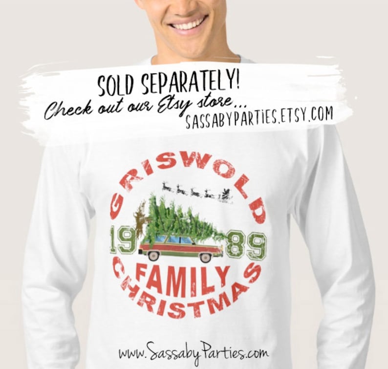 Pu&ograve; includere: Maglietta bianca a maniche lunghe con una grafica circolare rossa e verde che presenta il testo "Griswold Family Christmas 1989" e un'immagine di cartone animato di una station wagon con un albero di Natale in cima. La grafica include anche una piccola immagine di Babbo Natale e renne che volano nel cielo.