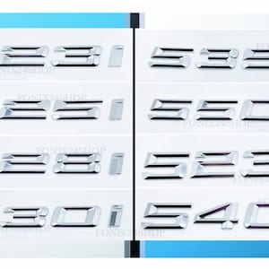 Könnte beinhalten: Eine Sammlung verchromter Autoembleme, darunter "535i", "535d", "530i" und "540d", auf weißem Hintergrund. Der Text "FONIX24SHOP" ist auf jedem Emblem zu sehen. Die Embleme sind wahrscheinlich für die Fahrzeuganpassung gedacht.