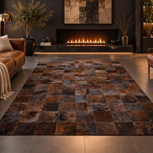 Puede incluir: Una alfombra rectangular compuesta por un mosaico de piezas de cuero cuadradas en varios tonos de marrón, bronceado y gris carbón oscuro. La alfombra presenta un patrón de cuadrícula con variaciones de color naturales en cada pieza.