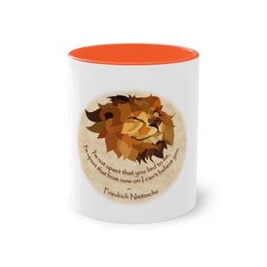 Peut inclure: Un mug en céramique blanc avec un intérieur et un bord orange vif. L'avant présente une illustration stylisée de lion brun centrée sur un fond circulaire beige, accompagnée du texte : I'm not upset that you lied to me, I'm upset that from now on I can't believe you. ~ Friedrich Nietzsche.