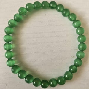 May include: A green beaded bracelet. The bracelet is made of round, polished beads in a vibrant green color. The beads are strung together to form a circular shape. The bracelet is displayed on a white surface.