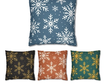 May include: Four square throw pillows with snowflake patterns. One pillow is blue with white snowflakes, another is black with gold snowflakes, a third is rust-colored with white snowflakes, and the last is green with gold snowflakes.