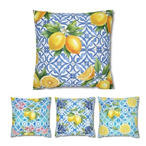 Puede incluir: Cojines cuadrados con diseños de acuarela. El cojín principal presenta un patrón de azulejos azules y blancos con limones y hojas verdes. Otros cojines tienen patrones similares con limones, flores y arándanos.